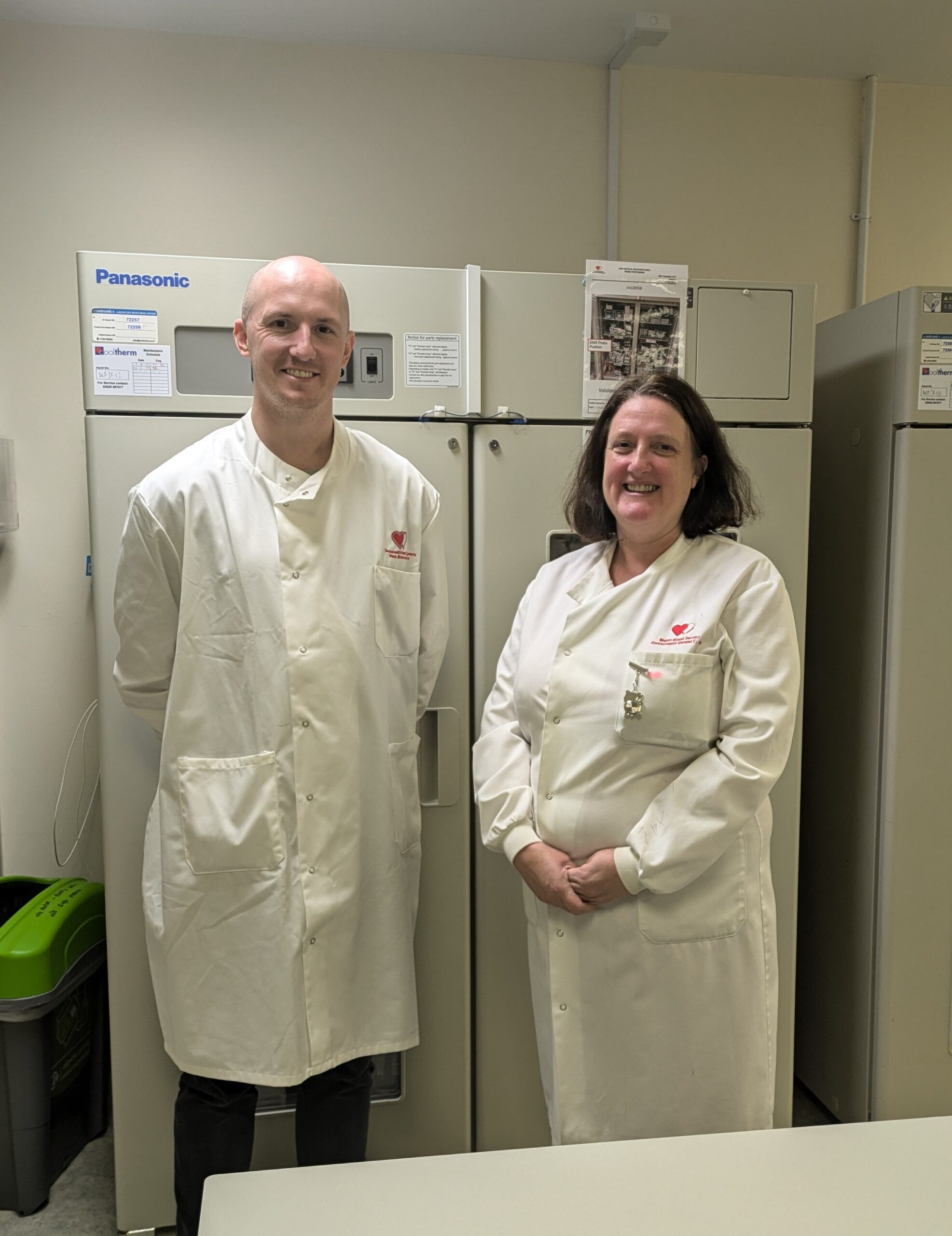 Dewi Reed and Ann Jones in lab coats standing in front of cabinets